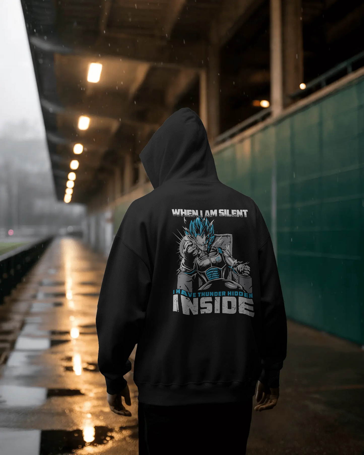 Person wearing a black hoodie with a graphic design and text under a bridge.