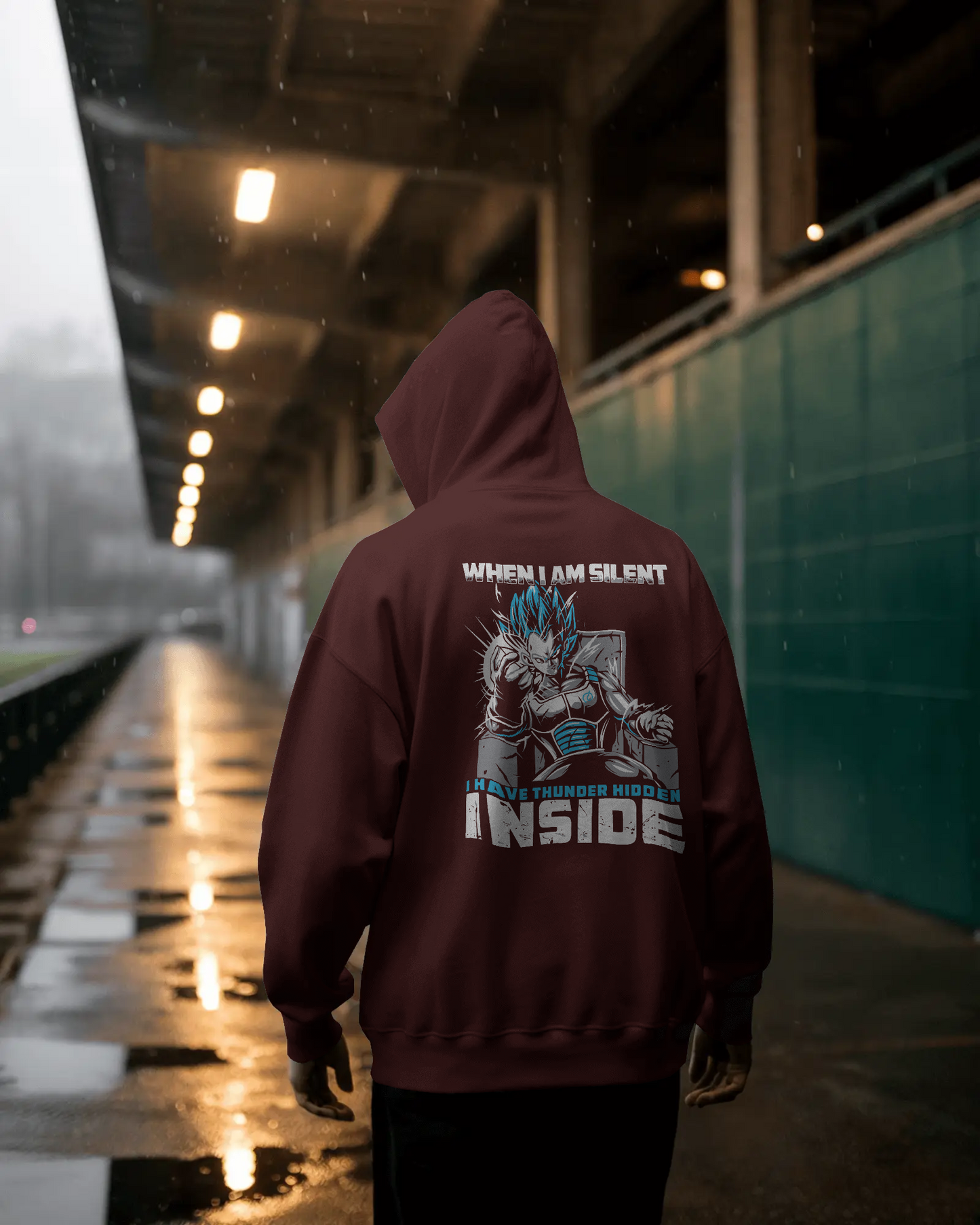Person wearing a maroon hoodie with a graphic design and text on the back, standing in a dimly lit area.