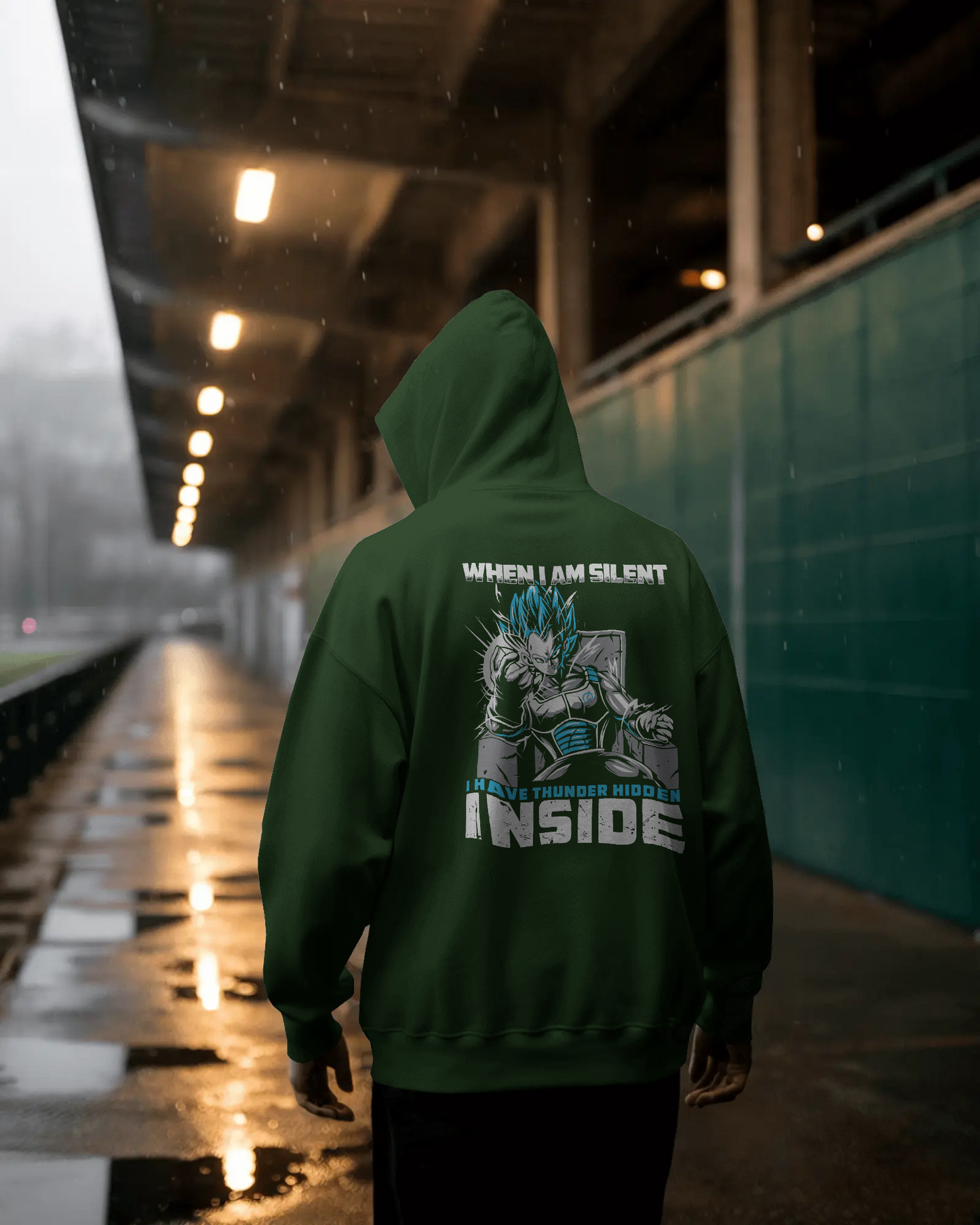 Person wearing a green hoodie with a graphic design and text under a bridge.